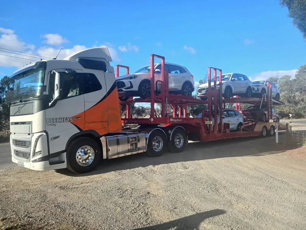 Beecheys Towing car carrier loaded with white vehicles on a gravel road