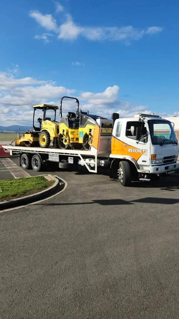 Beecheys Towing flatbed truck loaded with two yellow vibrating rollers on a sealed carpark in Launceston