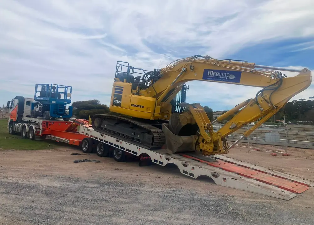 Low-loader truck transporting a Komatsu excavator with arm extended