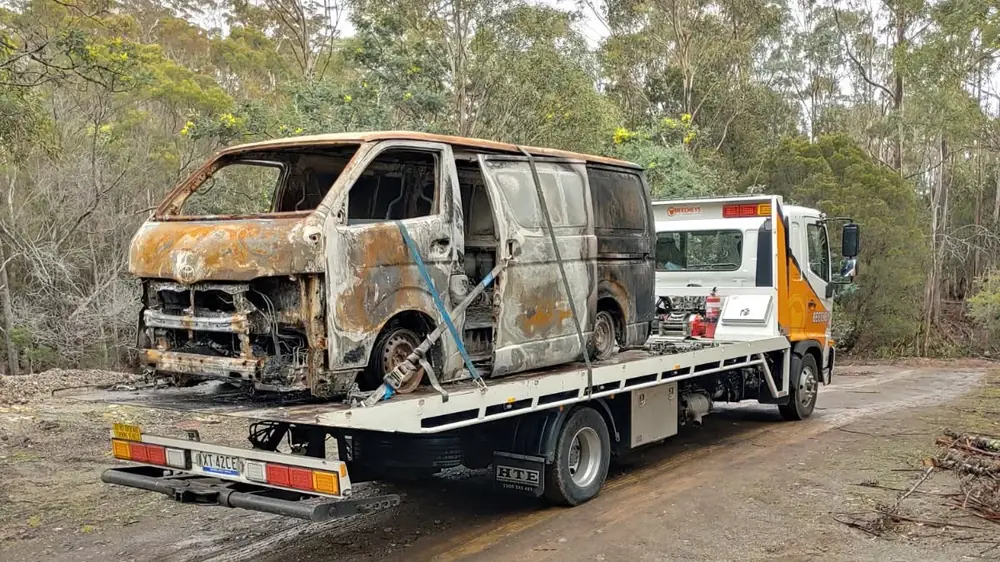 A burnt-out van being recovered onto a Beecheys Towing flatbed in bushland